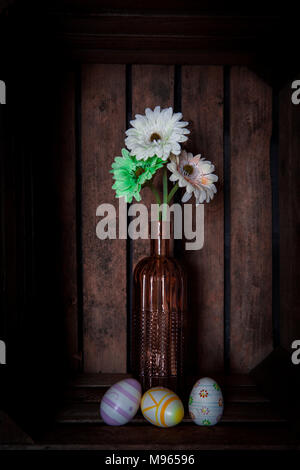 Easter eggs and spring flowers, gerbera or daisy, in a vintage pink vase inside an old wooden fruit crate Stock Photo
