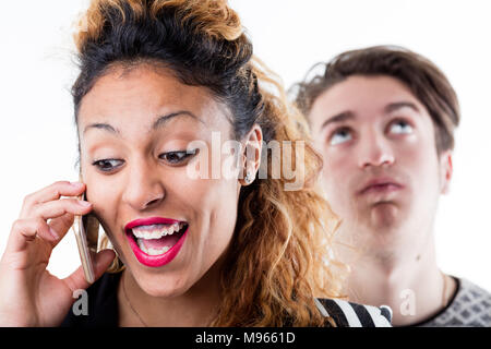 Young talkative woman talking on phone while impatient man standing in background Stock Photo