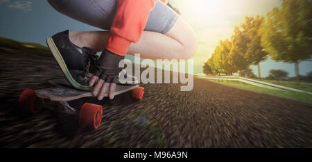 Man rides on a longboard in the street of a countryside environment with trees and blue sky. He drives with high speed experiencing the danger Stock Photo