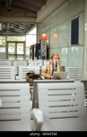 Young woman using her laptop at bus stop Stock Photo