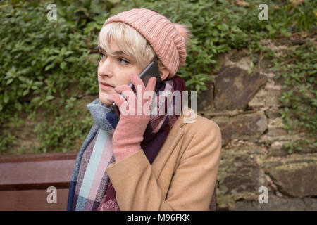 Young woman talking on phone while sitting on bench at park Stock Photo