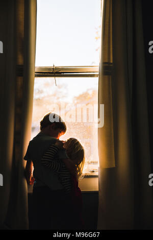 Children hugging next to dim window space Stock Photo