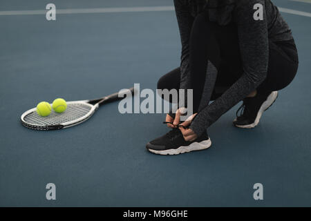 Woman tying her shoelaces in tennis court Stock Photo