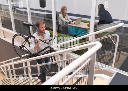 Male executive carrying cycle while moving upstairs Stock Photo