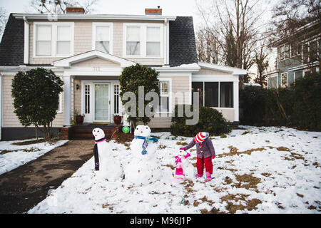 Girl standing next to line of three different snowman outside home Stock Photo