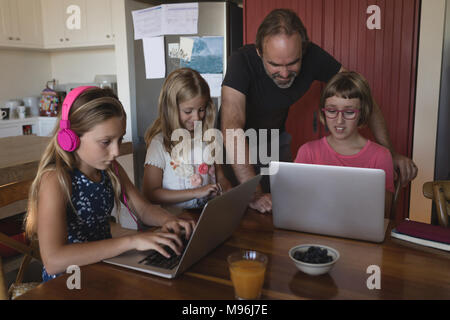Father and daughters using laptop in kitchen Stock Photo