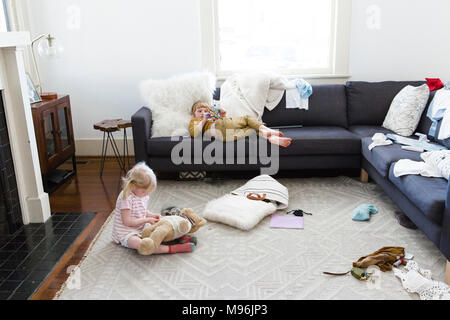 Girl laying on sofa with baby playing with bear on floor Stock Photo