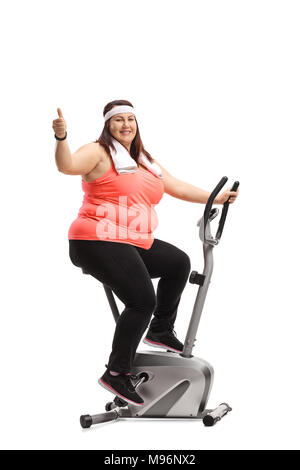 Overweight woman exercising on a stationary bike and making a thumb up gesture isolated on white background Stock Photo