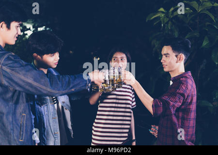 Asian group of friends having outdoor garden barbecue laughing with alcoholic beer drinks on night Stock Photo