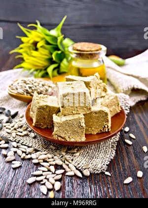 Eastern sweet halva sunflower in a plate, sunflower seeds, oil and flower on a sacking on a background of a dark wooden board Stock Photo