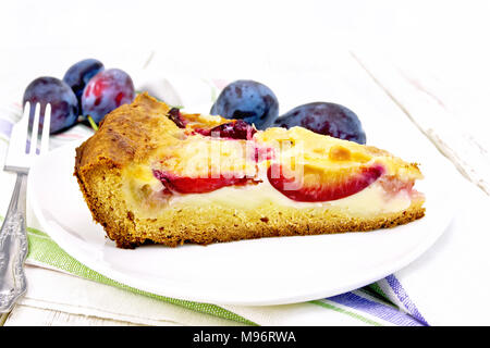Pie with plums and sour cream in a dish on a towel on a wooden plank background Stock Photo
