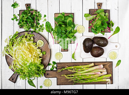 Green herbs, asparagus and black avocado on a white wooden background. Top view. Flat lay Stock Photo
