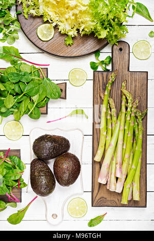 Green herbs, asparagus and black avocado on a white wooden background. Top view. Flat lay Stock Photo