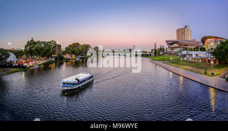 The Adelaide Skyline lights up at dusk reflecting in the serene River Torrens as tourists take a cruise on a pleasure boat. Stock Photo