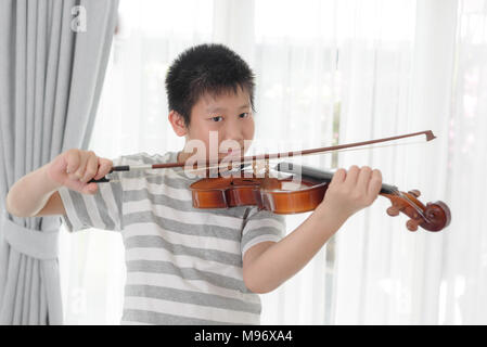 Happy Asian boy playing violin near window at home. Stock Photo