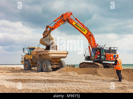 Excavator loading a dumper truck on a beach.