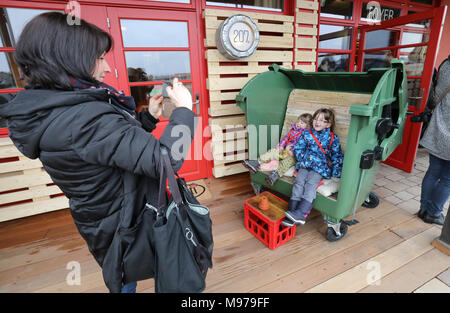 23 March 2018, Germany, Roevershagen: Mother Nicole Morawietz takes a picture of her children Marie (L-R) and Melina who sit on a garbage container which was upcycled into a seating furniture during a press event prior to the opening of the upcycling hotel 'Alles Paletti' (lit. everyhting is all right) at the Karls Erlebnis-Dorf (lit. Karl's Adventure Village). The hotel is meant to only consist out of upcycled materials. Photo: Bernd Wüstneck/dpa Stock Photo