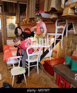 23 March 2018, Germany, Roevershagen: Mother Nicole Morawietz helps her children Melina (L-R) and Marie get down from the stairs made out of chairs during a press event prior to the opening of the upcycling hotel 'Alles Paletti' (lit. everyhting is all right) at the Karls Erlebnis-Dorf (lit. Karl's Adventure Village). The hotel is meant to only consist out of upcycled materials. Photo: Bernd Wüstneck/dpa Stock Photo