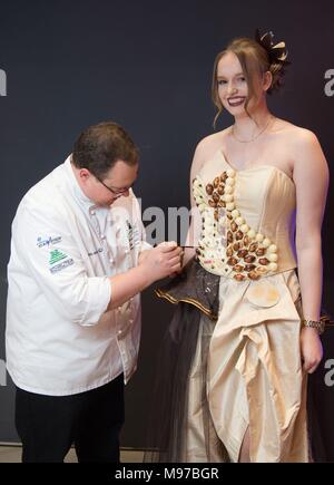 22 March 2018, Germany, Dresden: Master confectioner Jens Gradel works on the chocolate dress 'SchoCouture', which is worn by Astrid Stoecker, hairdresser trainee. The dress made of tulle and silk consists of altogether 160 pralines. The European Days of Arts and Craft are opened with the live performance on the same day. They take place from 23 to 25 March 2018 and run under the motto 'Kunsthandwerk zeigen - gemeinsam gestalten' (lit. showing arts and craft - craft together). Photo: Sebastian Kahnert/dpa Stock Photo