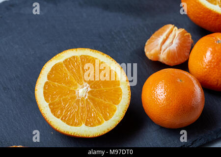 High angle still life view of sliced ruby orange and tangerine arranged together on the right side of black stone cutting board over white textured ba Stock Photo