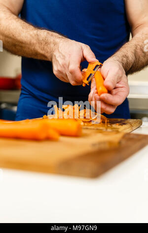 Man peeling carrots on a wooden board Stock Photo