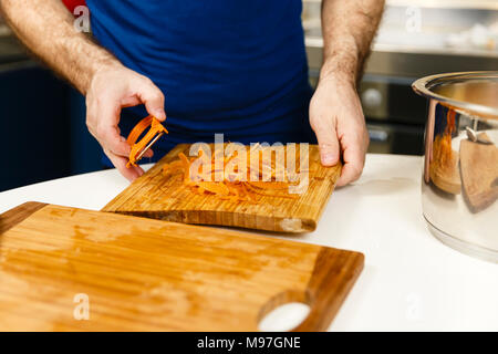 Man peeling carrots on a wooden board Stock Photo