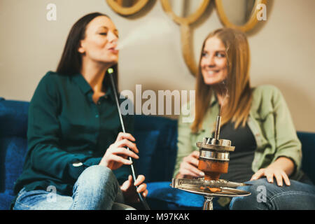 Two happy women are sitting in shisha bar and smoking nargile Stock Photo