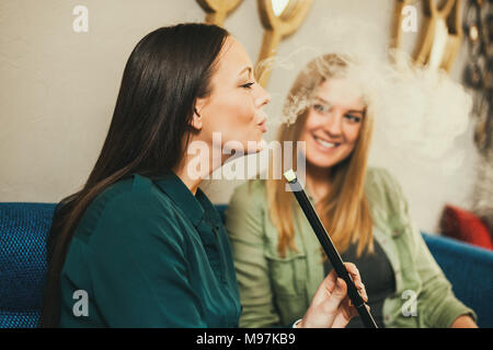 Two happy women are sitting in shisha bar and smoking nargile Stock Photo