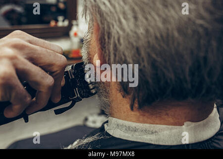 Close-up side back view handsome senior bearded caucasian man getting beard grooming in modern barbershop. Hairdresser serving client, making beard ha Stock Photo