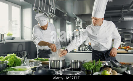 Two Famous Chefs Work as a Team in a Big Restaurant Kitchen. Vegetables and Ingredients are Everywhere, Kitchen Looks Modern. Stock Photo