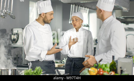 In the Modern Kitchen Team of Cooks Have Discussion. Kitchen is Full of Food Ingredients, Vegetables, Meat, Boiling Soup. Stock Photo