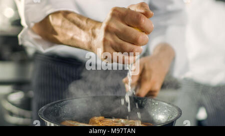 Professional Chef Squeezes Lemon Juice onto Hot Pan with Red Fish Fillet on it. He Works in a Modern Kitchen. Stock Photo