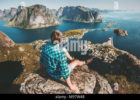 Man sitting on mountain top cliff above sea and rocks lifestyle travel adventure outdoor summer vacations tourist enjoying aerial view in Norway Lofot Stock Photo