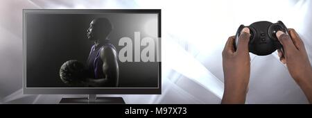 Hands holding gaming controller  with basketball on television Stock Photo