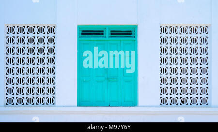 Old, antique turquoise door flanked by full-size arabic pattern windows - Muscat, Oman. Stock Photo