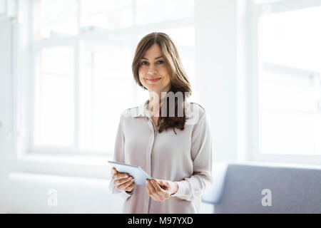 Portrait of smiling woman standing in bright room holding tablet Stock Photo