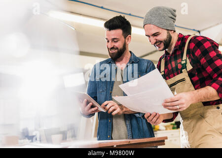 Two happy men with tablet looking at draft in workshop Stock Photo