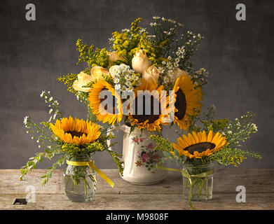 Sunflowers in antique jug and jam jars Stock Photo