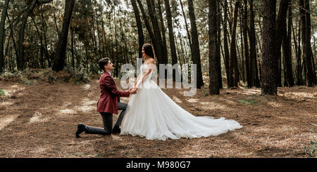 Man kneeling making a marriage proposal to happy bride in forest Stock Photo