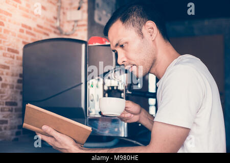 Handsome man drinking coffee and reading book at coffee shop Stock Photo