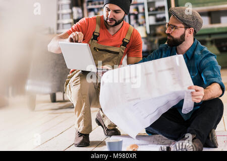 Two men with tablet looking and draft sitting on the floor Stock Photo