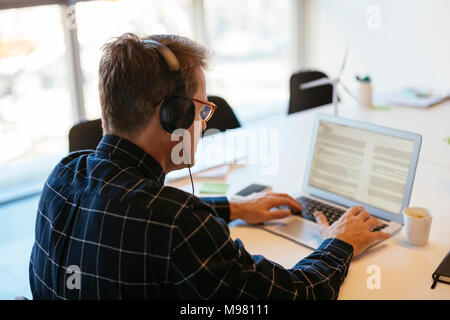 Businessman wearing headphones using laptop at desk in office Stock Photo