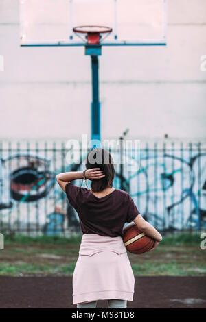 Rear view of young woman standing with basketball on outdoor court Stock Photo
