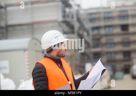 Man with plan wearing safety vest and hard hat at construction site Stock Photo