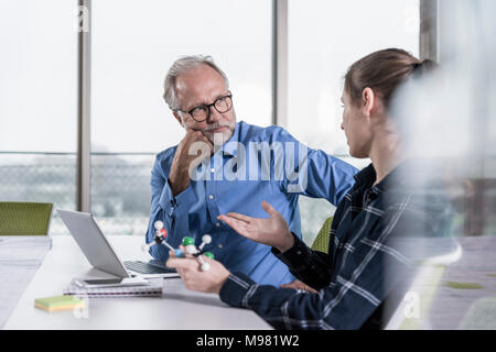 Mature businessman and young woman with atomic model talking in conference room Stock Photo