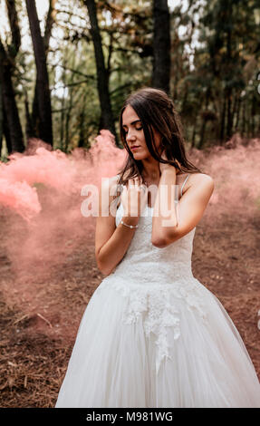 Woman with closed eyes wearing wedding dress in forest surrounded by clouds of smoke Stock Photo