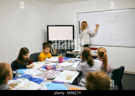 Teacher writing on whiteboard in class Stock Photo