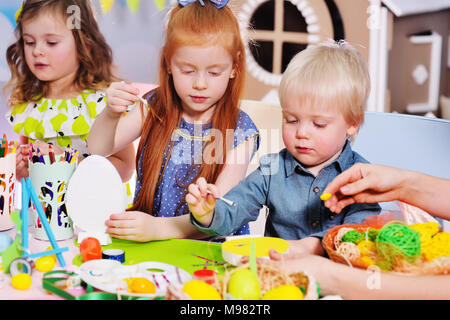 children in kindergarten paint eggs for the Easter basket at the table. Preparation for the celebration of Easter. Stock Photo