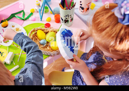 children in kindergarten paint eggs for the Easter basket at the table. Preparation for the celebration of Easter. Stock Photo