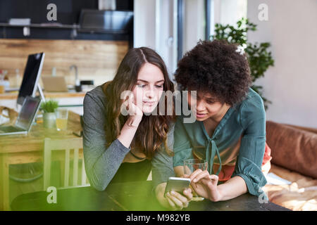 Two young women sharing cell phone in modern office Stock Photo